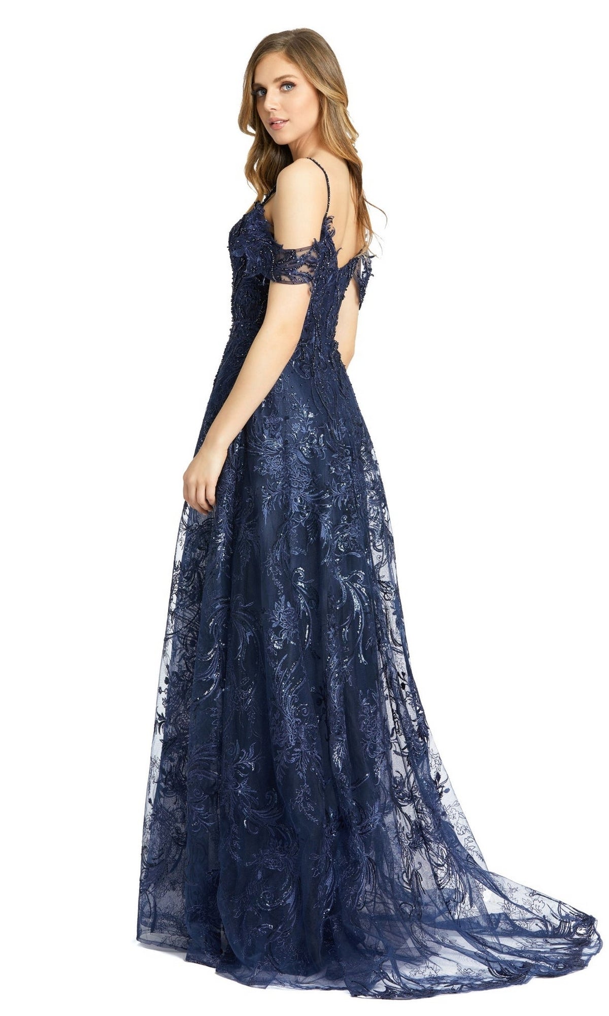A woman stands, looking over her shoulder, wearing the Long Formal Dress 20287 by Mac Duggal—a navy blue off-shoulder gown with lace details and a sweetheart neckline.